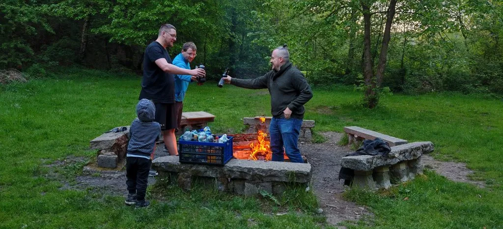 Vereinsmitglieder stoßen abends an einer Feuerstelle im Grünen an