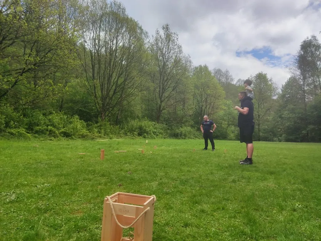 Familien spielen ein Wurfspiel aus Holz auf einer Wiese am Waldrand